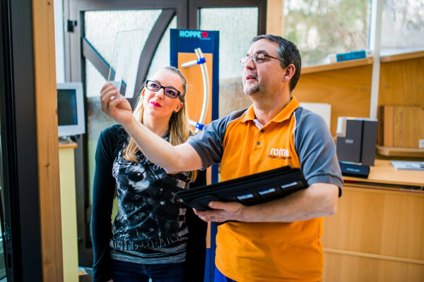 Ein Fachberater erklärt einer Kundin im Geschäft die Auswahl moderner Fensterprofile.