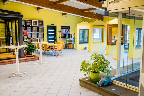 Heller Ausstellungsraum mit modernen Fenstern, Türen, Sitzbereich und Dekopflanzen.